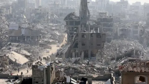 Reuters People walk past the rubble of destroyed buildings, inJabalia, in the northern Gaza Strip, on 30 January 2025