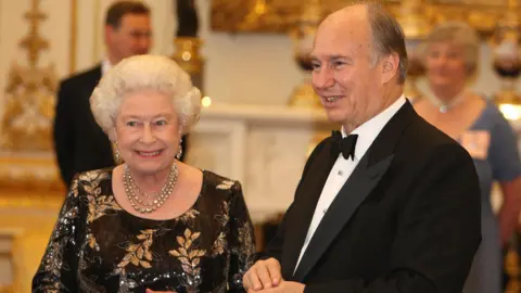 PA Media Queen Elizabeth II wearing a black dress with golden leaf patterns standing next to the Aga Khan wearing a black tuxedo