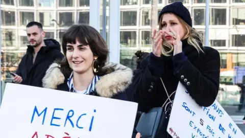 EPA Two women holding signs written in French in support of the actor Adèle Haenel. The woman on the right is clapping and behind them a man looks on.